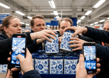 En Kaotisk Scen I En Svensk Mataffär, Där En Folkmassa Av Kunder Knuffas Och Sträcker Sig För Att Nå Blåblommiga Mon Amie-Kaffeburkar, Med Smartphones Som Filmar Händelsen, Vilket Illustrerar Fomo-Kultur (Fear Of Missing Out) Och Konsumtionshysteri.